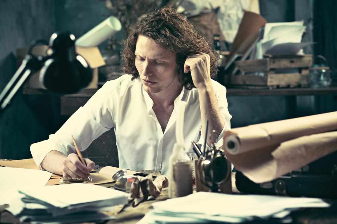 Хлопець за письмовим столом пише пером рядка на аркушах паперу