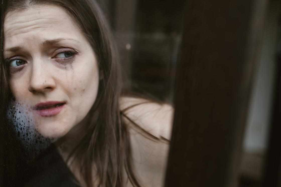 Засмучена дівчина із заплаканим обличчям стоїть біля вікна