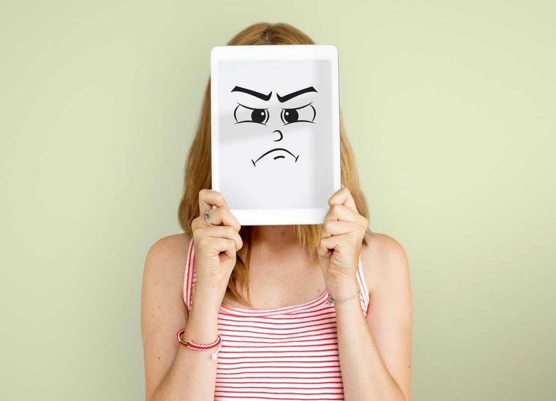 Дівчина тримає планшет перед обличчям із зображенням сумної пики